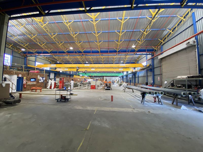 Spacious industrial warehouse facility featuring high ceilings with exposed steel trusses, overhead bridge cranes, and large roller shutter access doors.