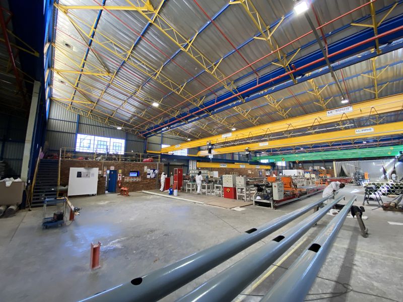Spacious industrial warehouse facility featuring high ceilings with exposed steel trusses, overhead gantry cranes, and durable concrete flooring suitable for manufacturing or storage operations.