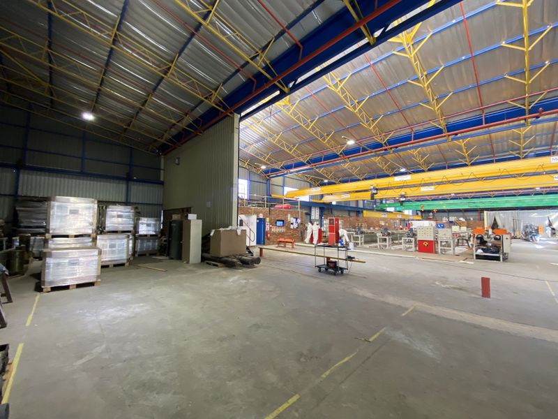 Spacious industrial warehouse facility featuring high-clearance exposed steel roof trusses, overhead gantry crane, and durable concrete flooring suitable for manufacturing or storage operations.