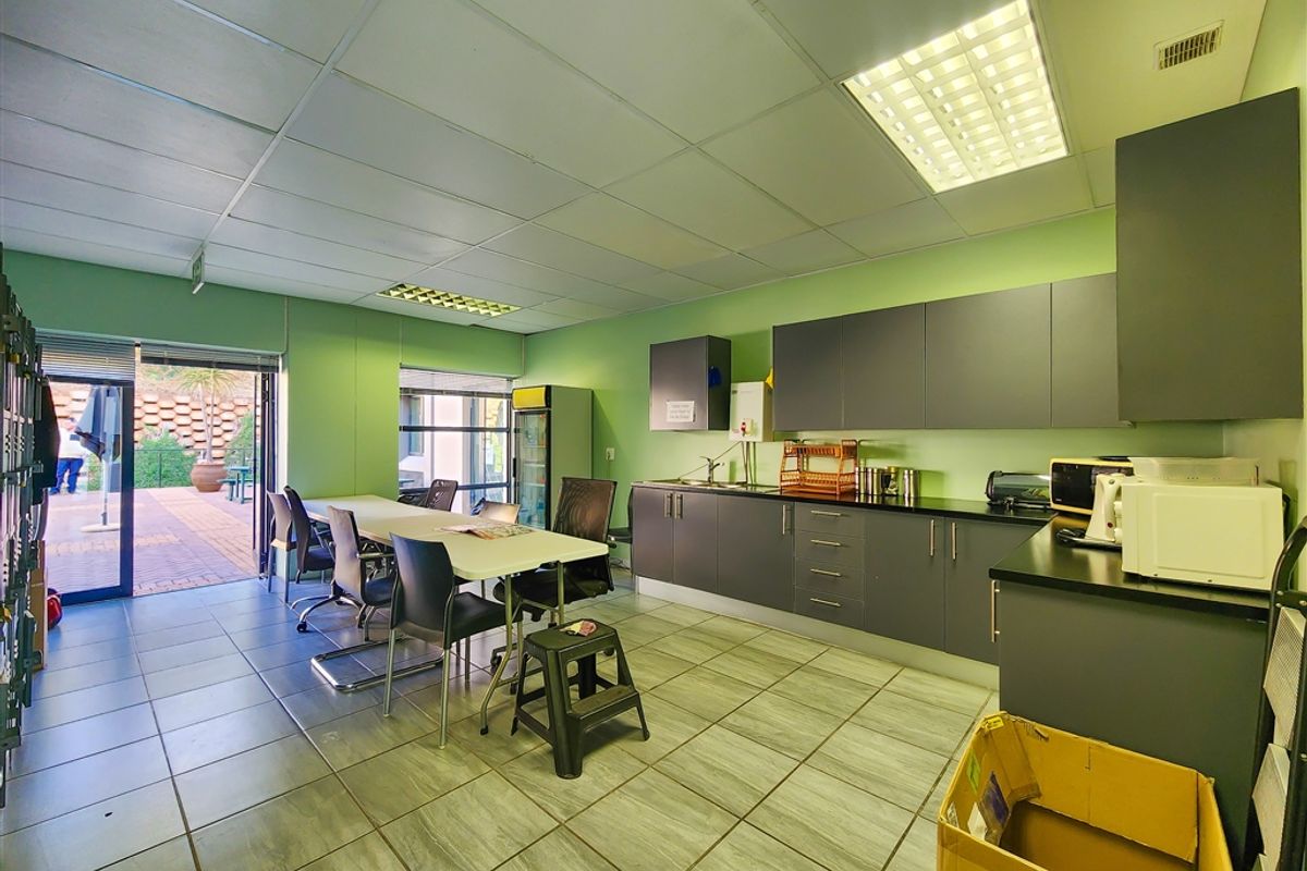 A functional office kitchenette featuring dark grey cabinetry, a stainless steel sink, and direct access to an outdoor patio area.
