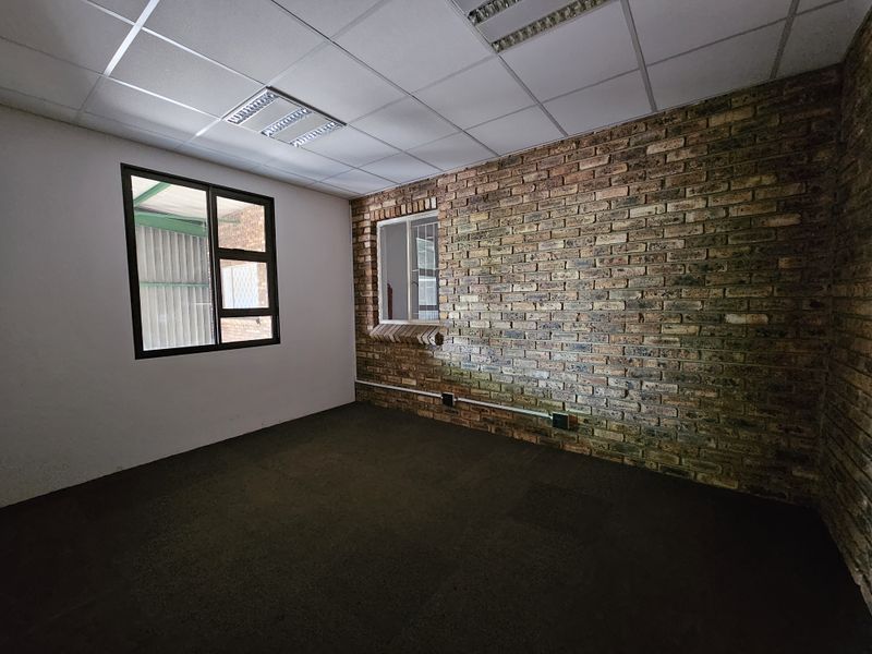 An empty office space featuring an exposed brick feature wall, suspended ceiling with recessed lighting, and carpeted flooring.