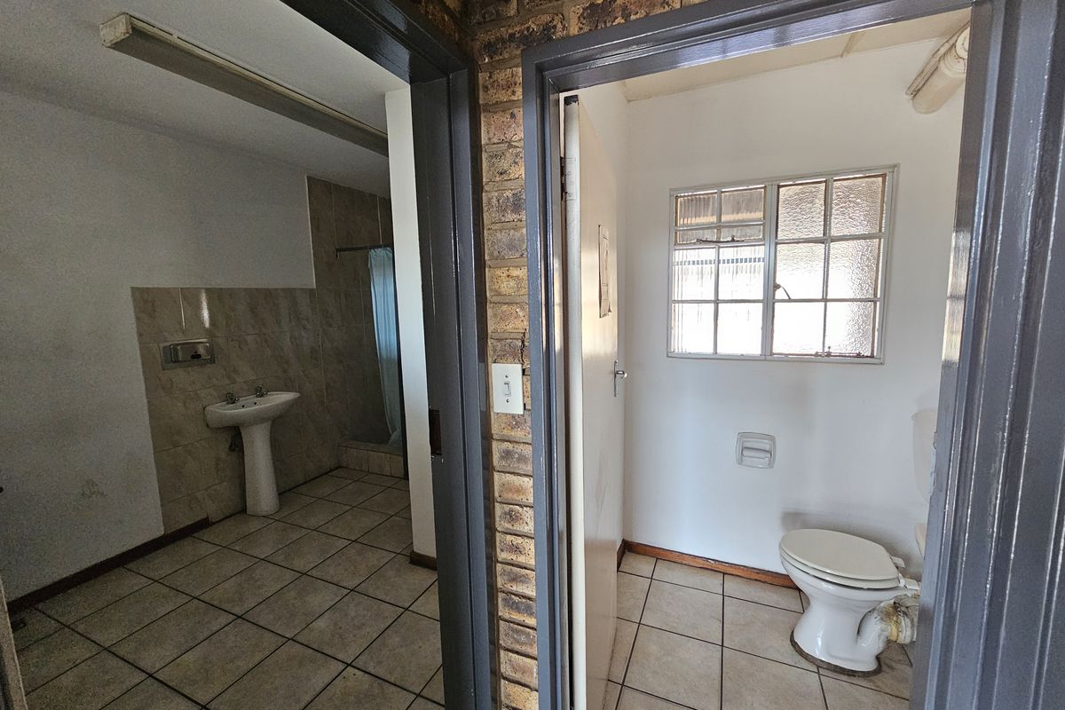 A functional bathroom area featuring a pedestal basin and separate toilet, with tiled flooring and exposed brick accents, ready for modernization.