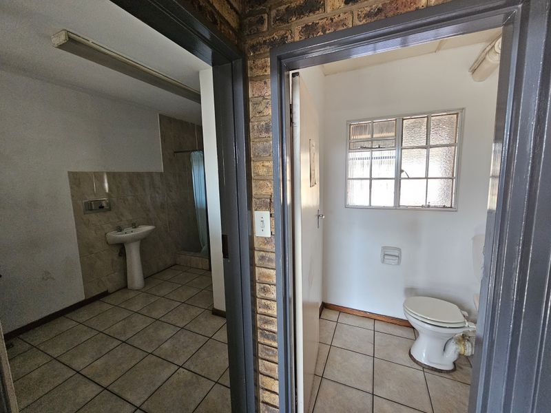 A functional bathroom area featuring a pedestal basin and separate toilet, with tiled flooring and exposed brick accents, ready for modernization.