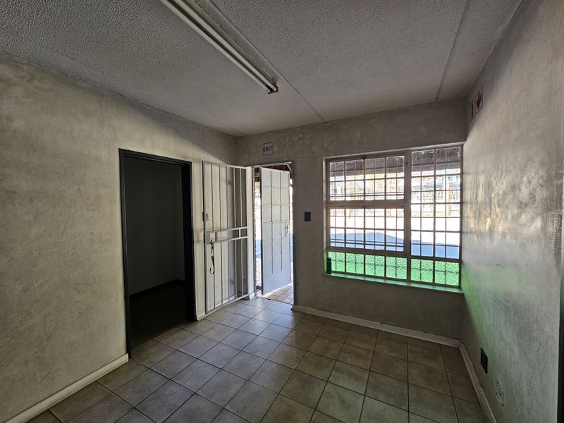 An empty office space featuring tiled flooring, fluorescent lighting, and a security gate, providing a functional and secure workspace environment.