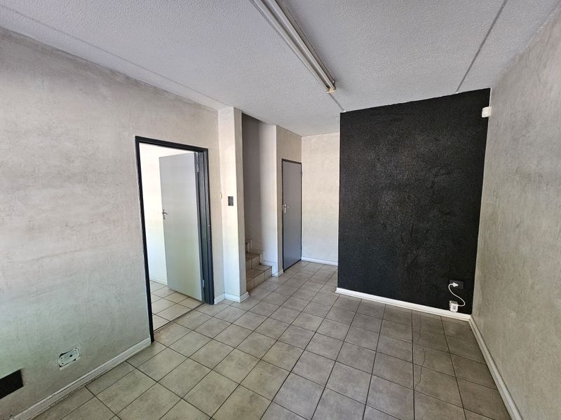 An empty industrial office space featuring ceramic tiled flooring, fluorescent lighting, and a staircase leading to an adjacent area.