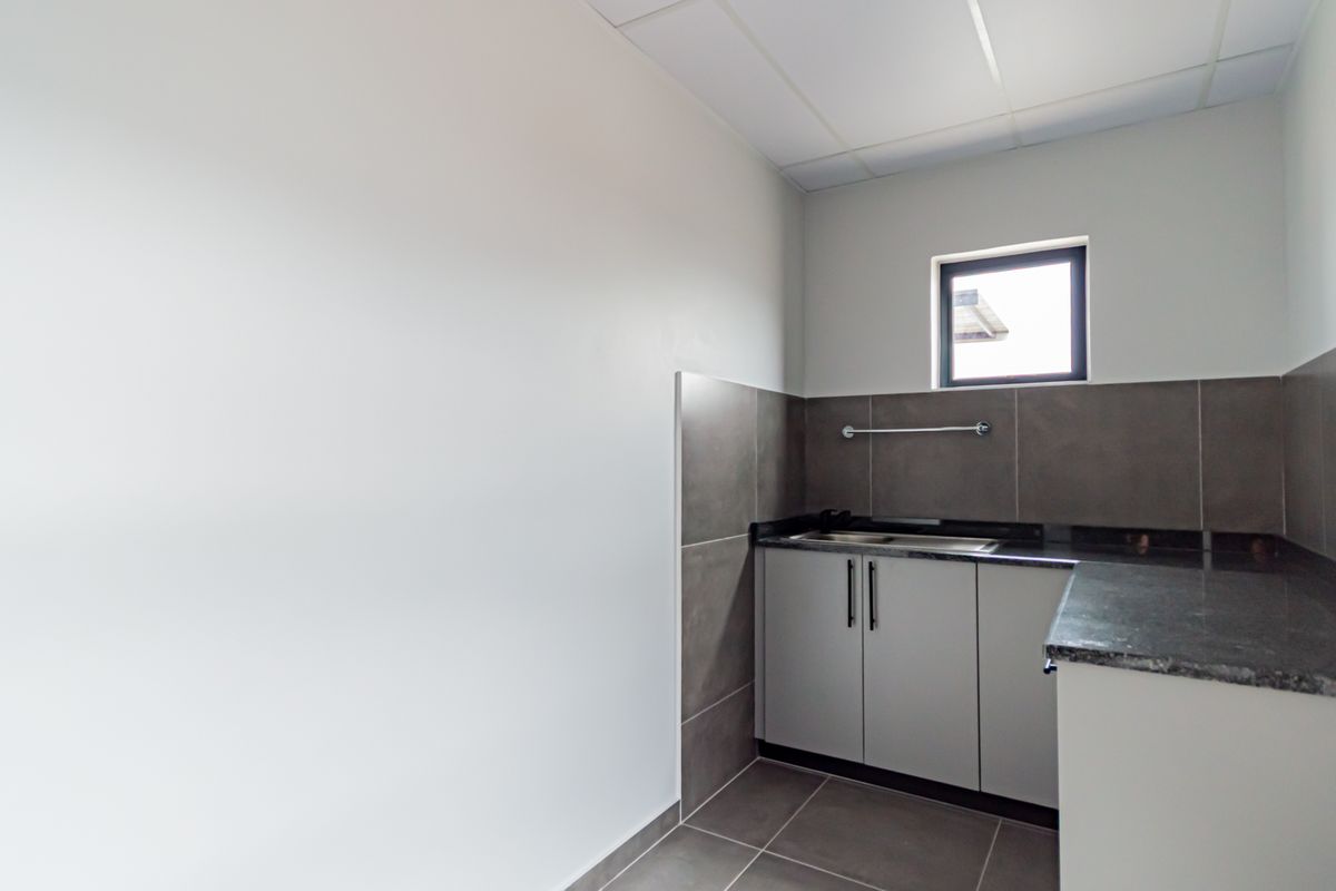 A clean, modern kitchenette area featuring grey cabinetry, dark stone countertops, tiled splashbacks, and a stainless steel sink.
