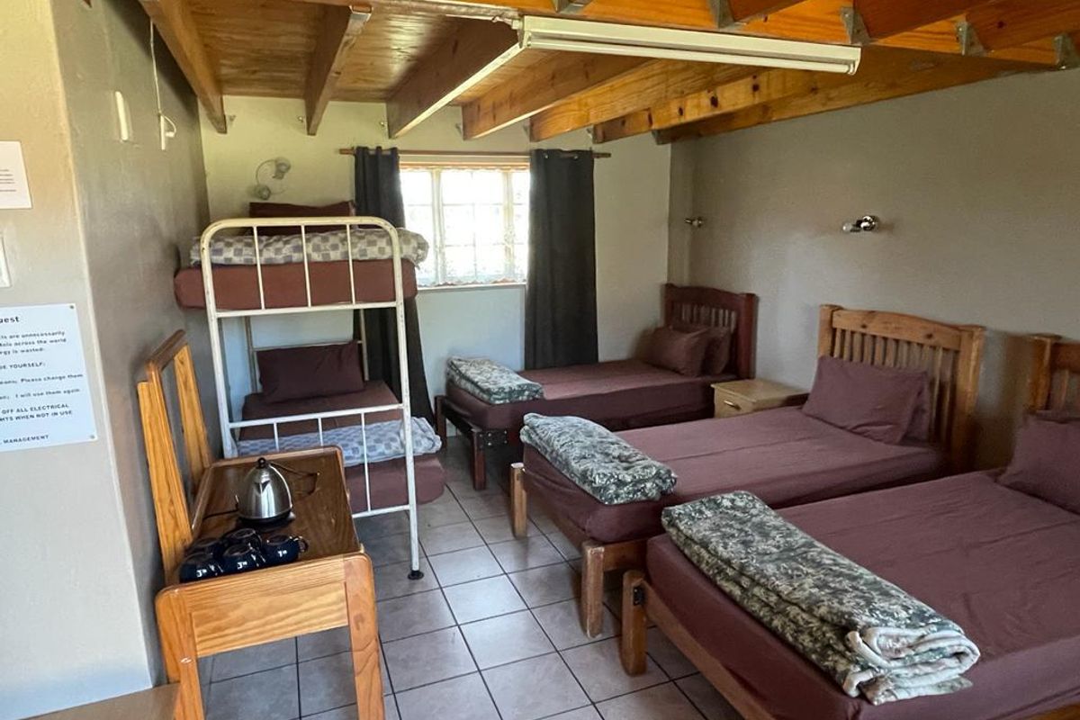 A functional lodge bedroom featuring multiple beds, exposed timber ceiling beams, and tiled flooring, providing practical accommodation space.