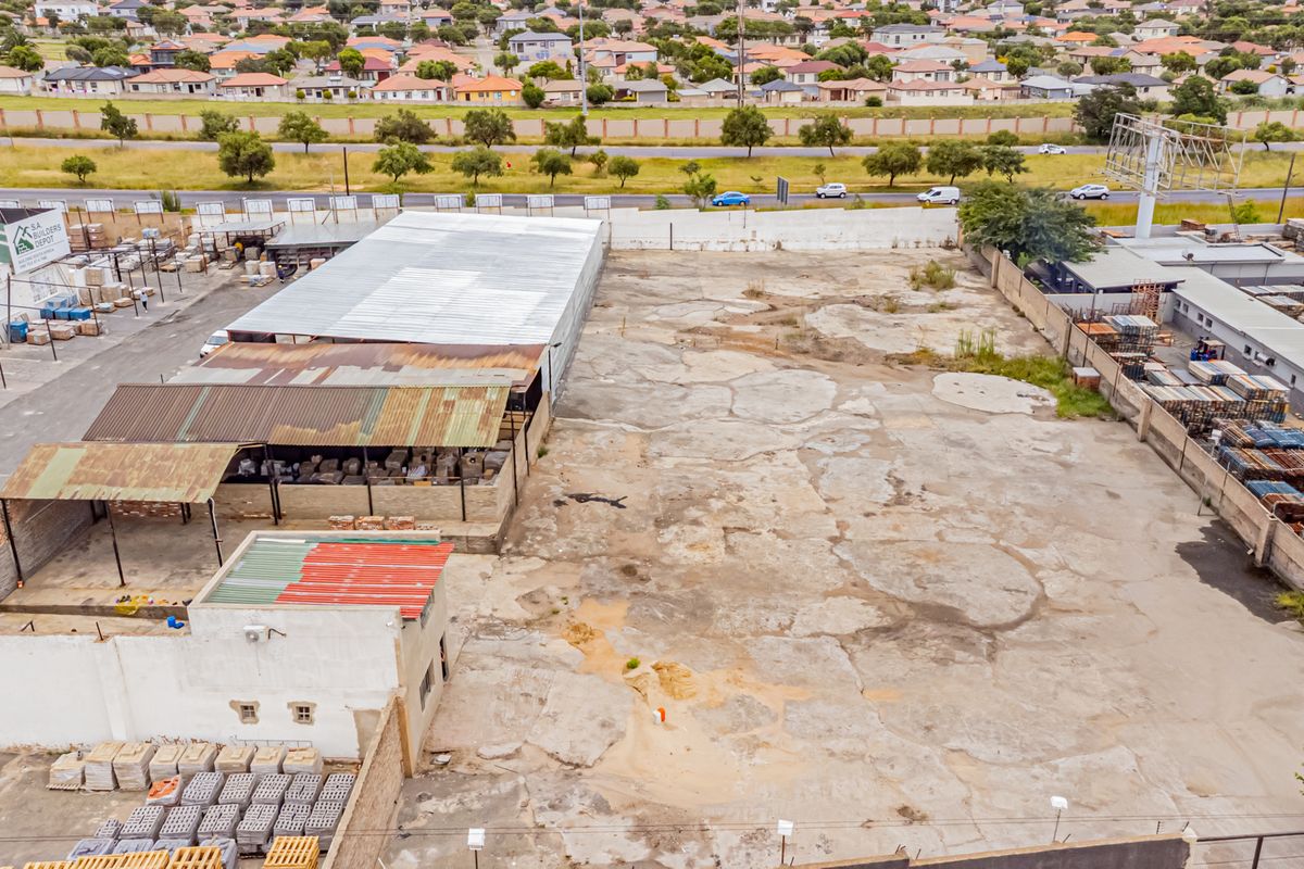 Aerial view of a commercial property featuring a large concrete yard, industrial storage structures with metal roofing, and perimeter boundary walls.