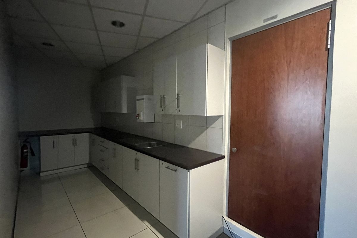 A functional office kitchenette featuring white cabinetry, dark countertops, a stainless steel sink, and tiled flooring.
