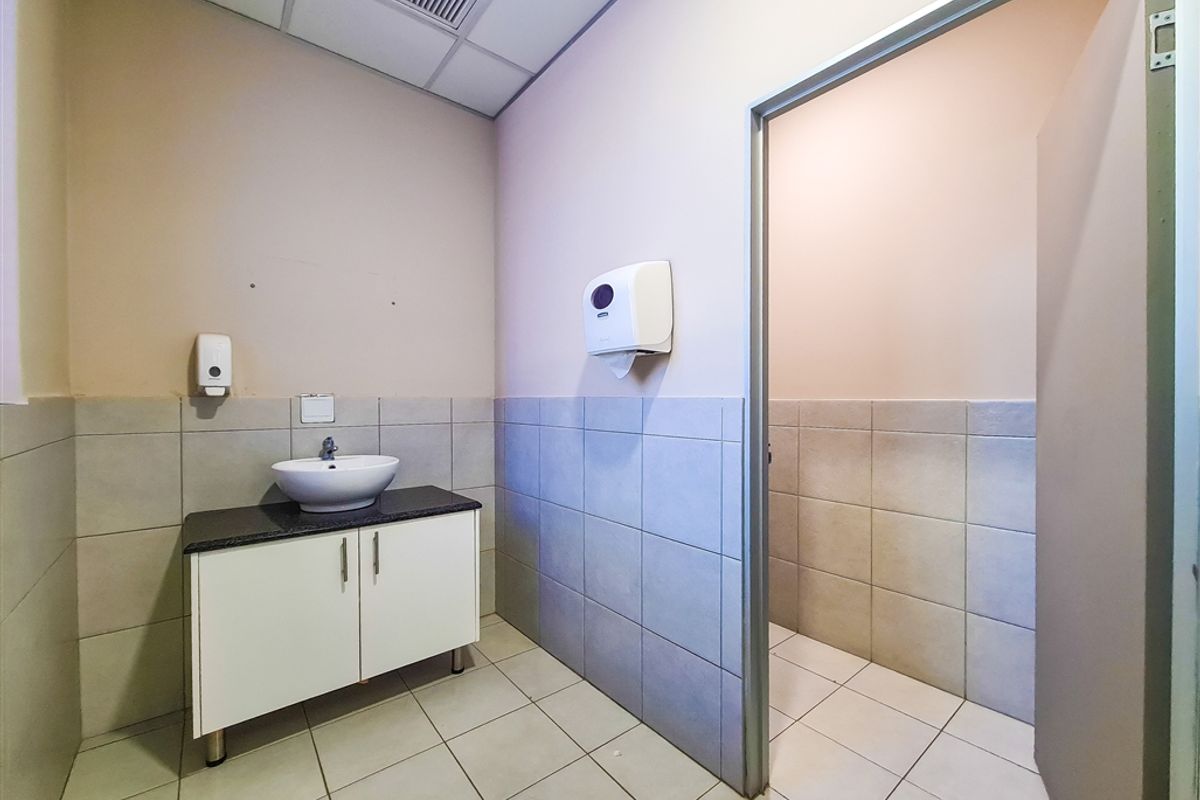 A functional office restroom featuring a vanity cabinet with a vessel sink, tiled flooring, and half-tiled walls.