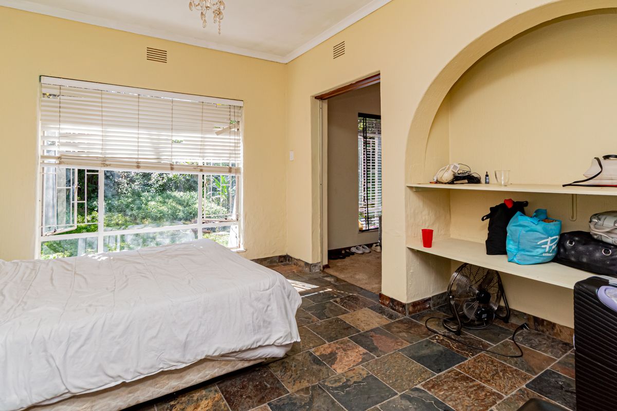 A bedroom featuring natural stone flooring, a built-in arched shelving unit, and large windows overlooking the garden.