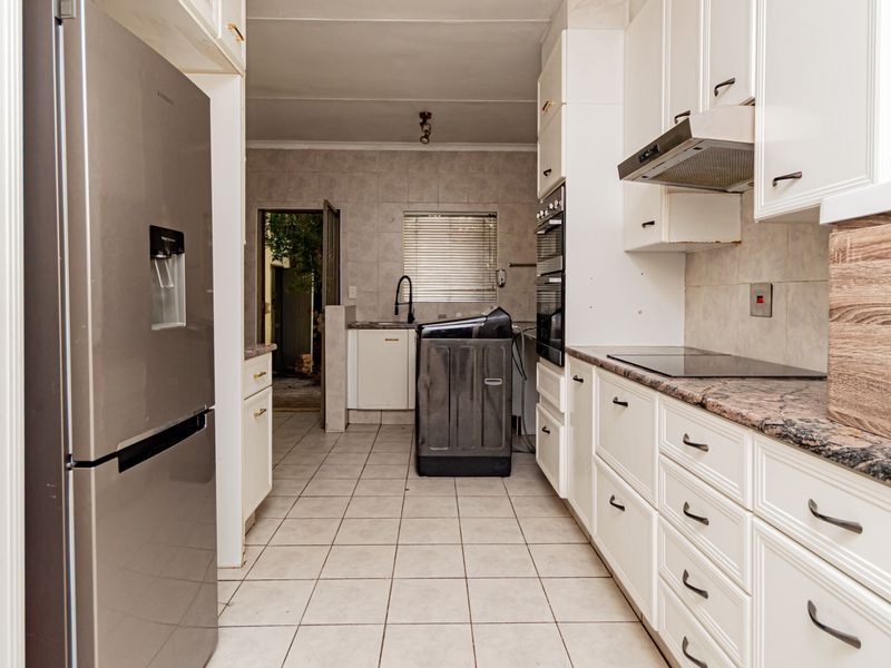 A functional kitchen featuring white cabinetry, stone-look countertops, a built-in oven, and a tiled floor, leading to a secondary utility or prep area.