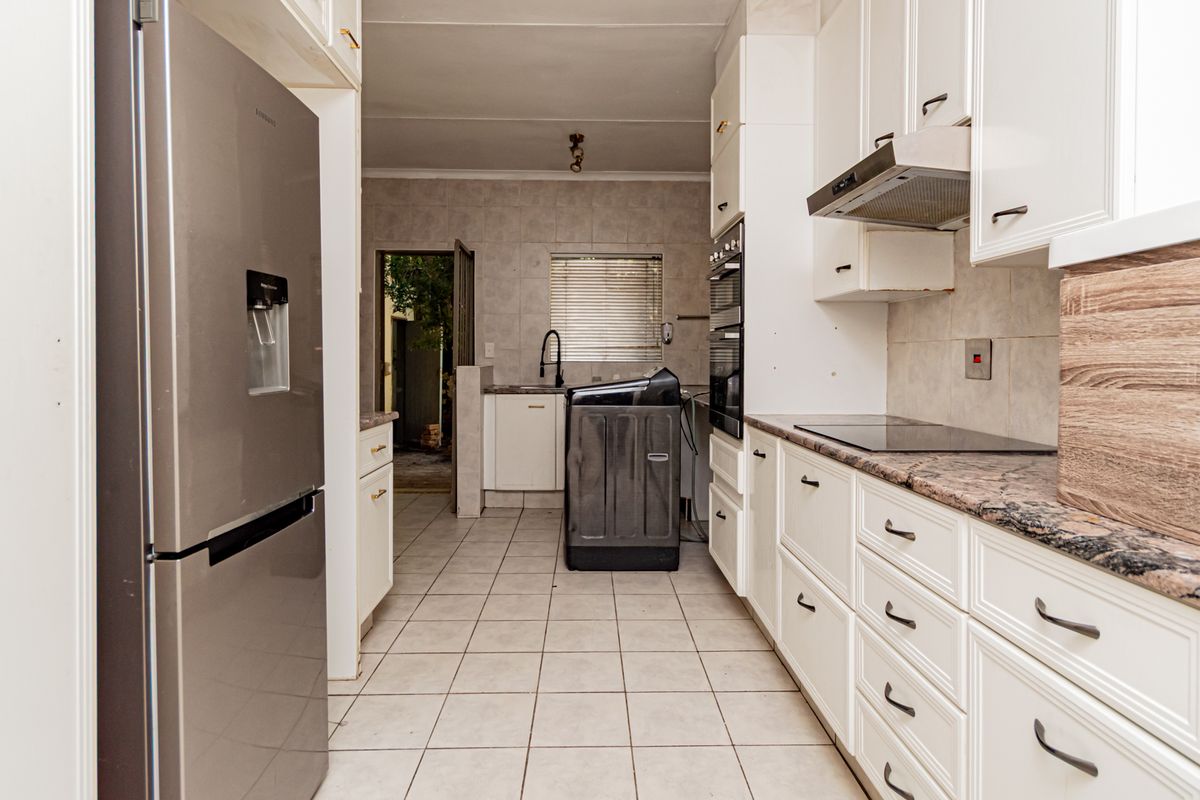 A functional kitchen featuring white cabinetry, stone-look countertops, a built-in oven, and a tiled floor, leading to a secondary utility or prep area.