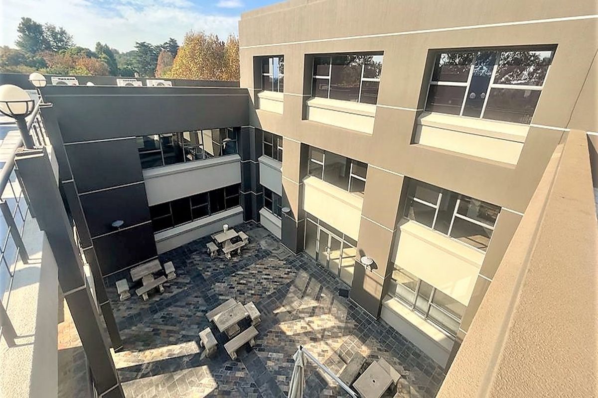An elevated view of a paved outdoor courtyard area situated between office building wings, featuring stone-tiled flooring and integrated exterior lighting.