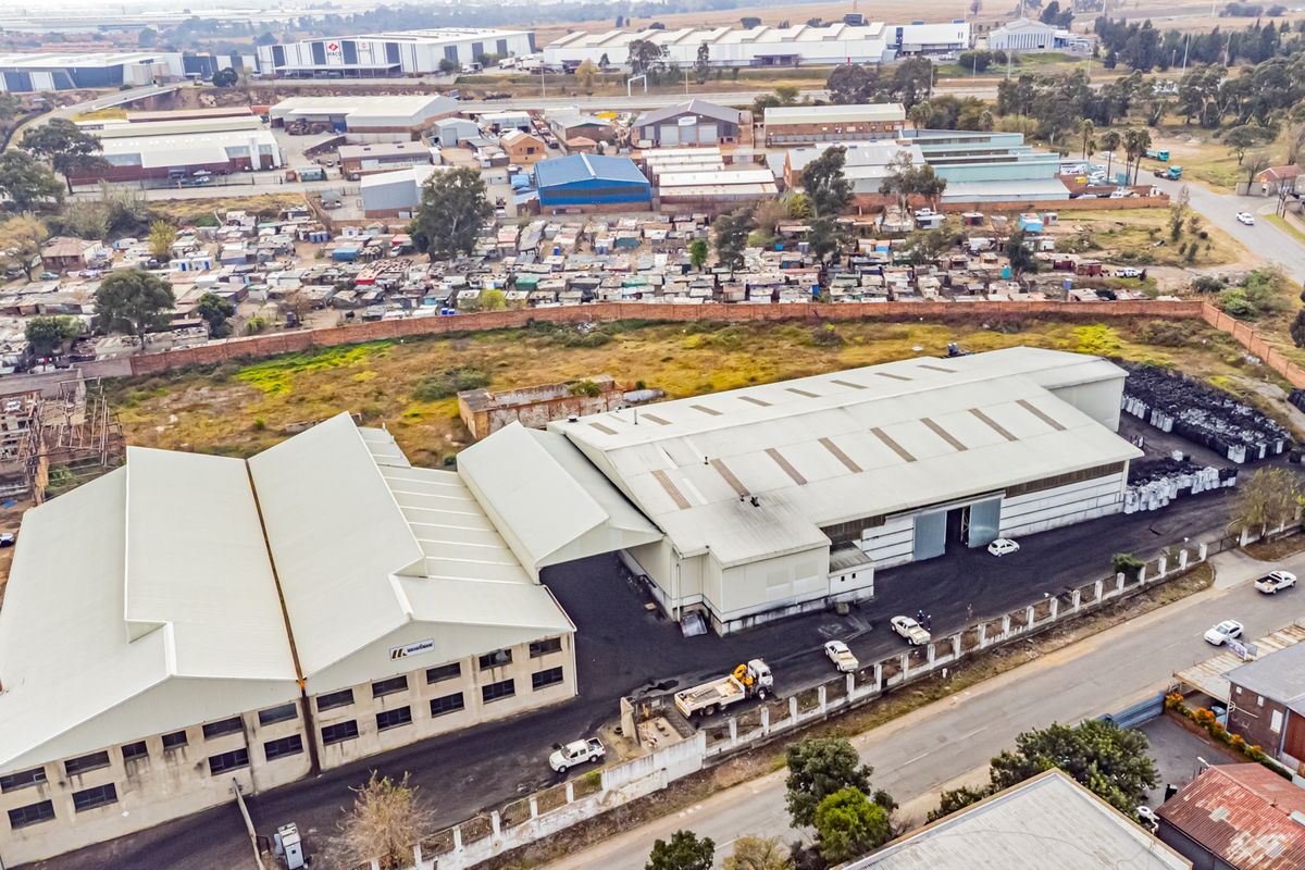 Aerial view of a large industrial warehouse facility featuring expansive metal roofing, paved yard space, and secure perimeter fencing in an industrial zone.