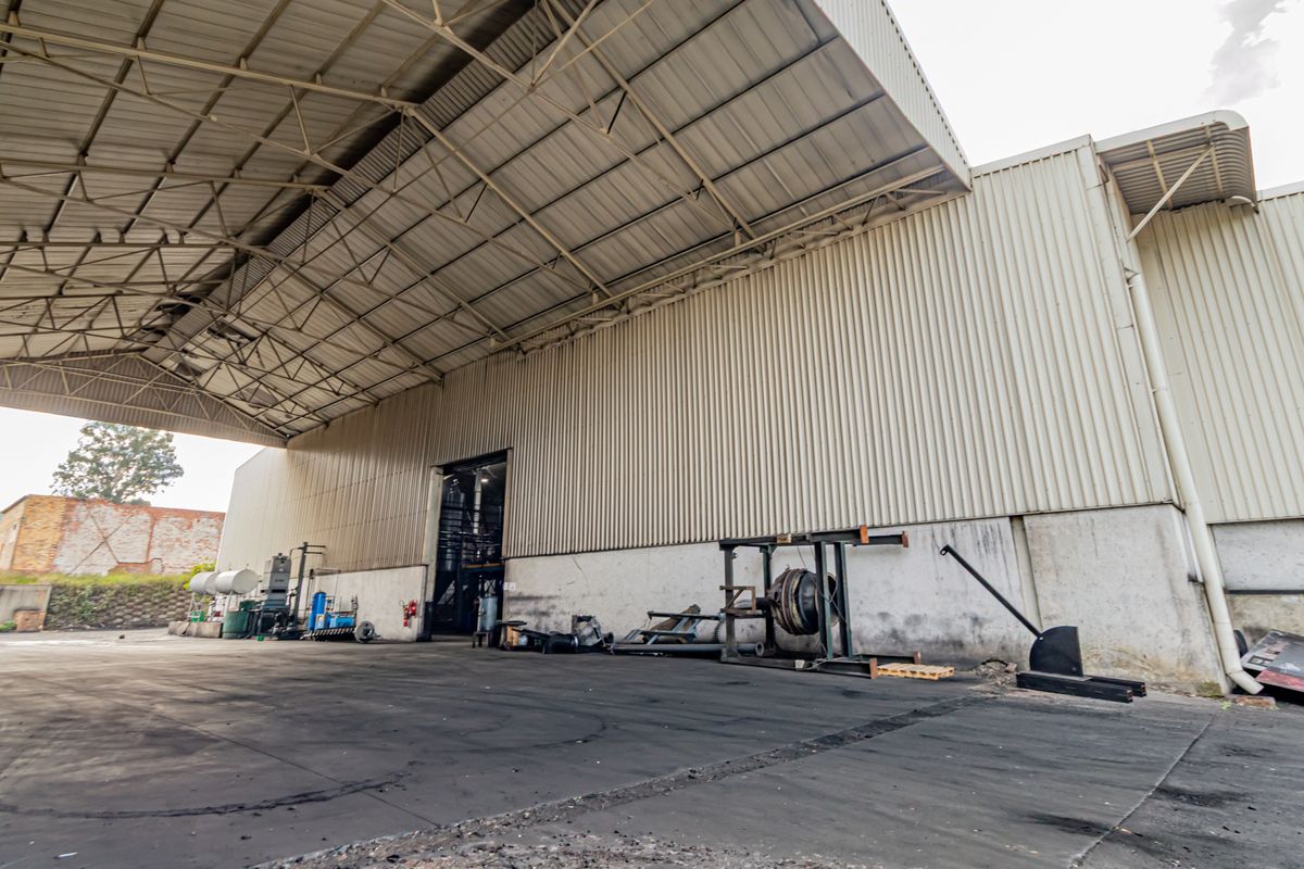 Large industrial warehouse exterior featuring a covered loading area, corrugated metal cladding, and expansive concrete hardstand suitable for heavy vehicle access.
