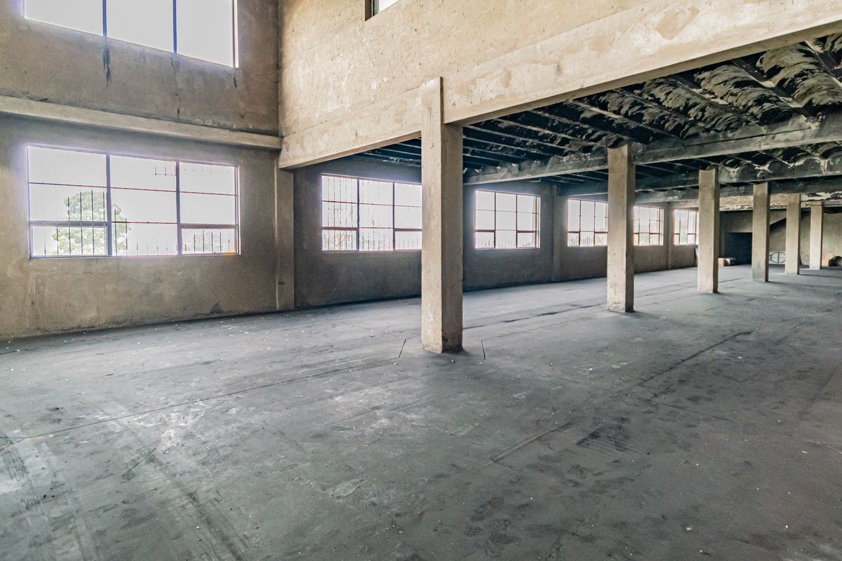Expansive industrial utility space featuring high ceilings, concrete columns, and large steel-framed windows, offering a blank canvas for redevelopment or storage.