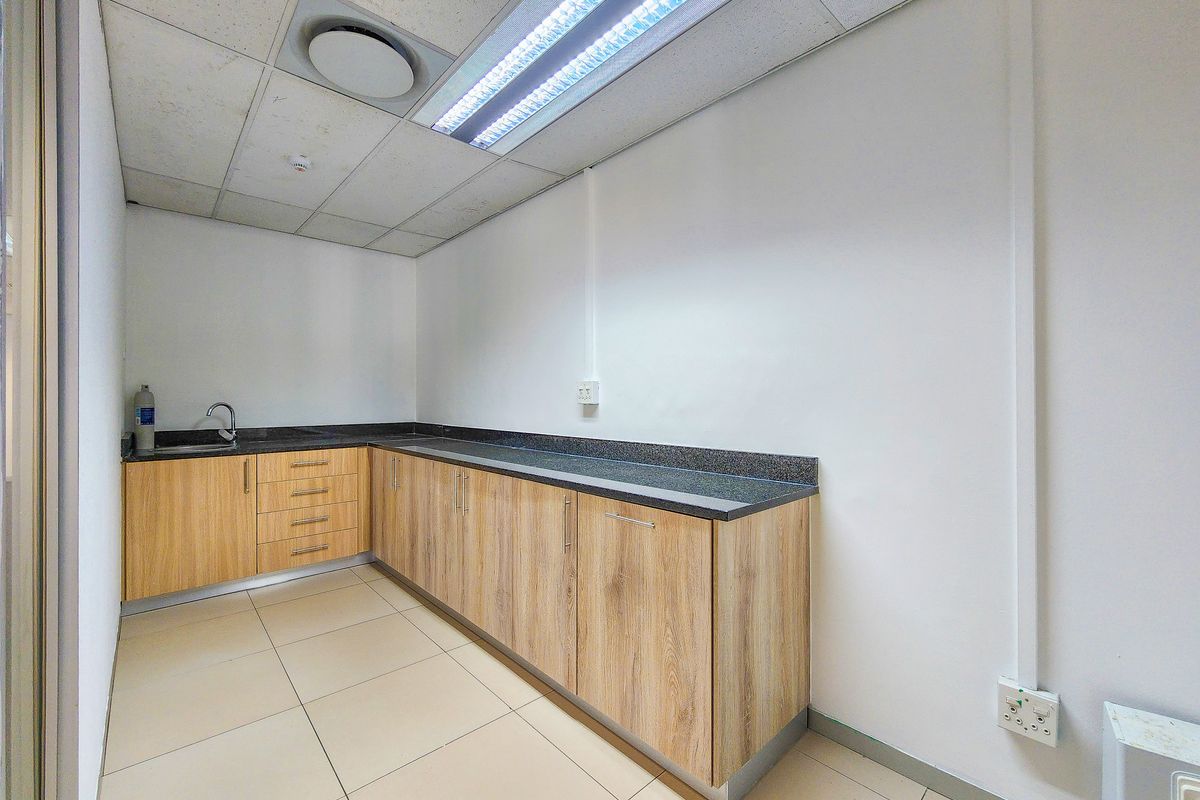 A clean, functional office kitchenette featuring light wood-grain cabinetry, dark granite countertops, a stainless steel sink, and modern drop ceiling lighting.