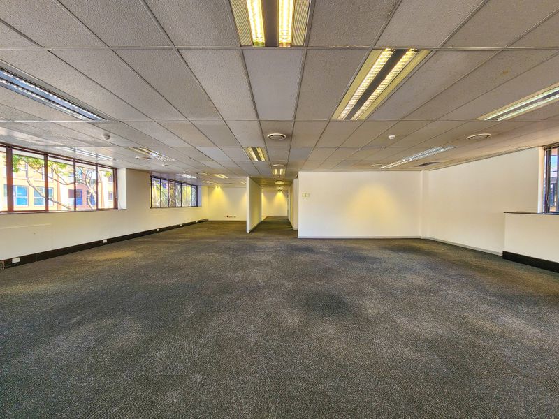 A spacious, open-plan office area featuring suspended ceilings, recessed lighting, and large windows providing natural light, ready for custom fit-out.