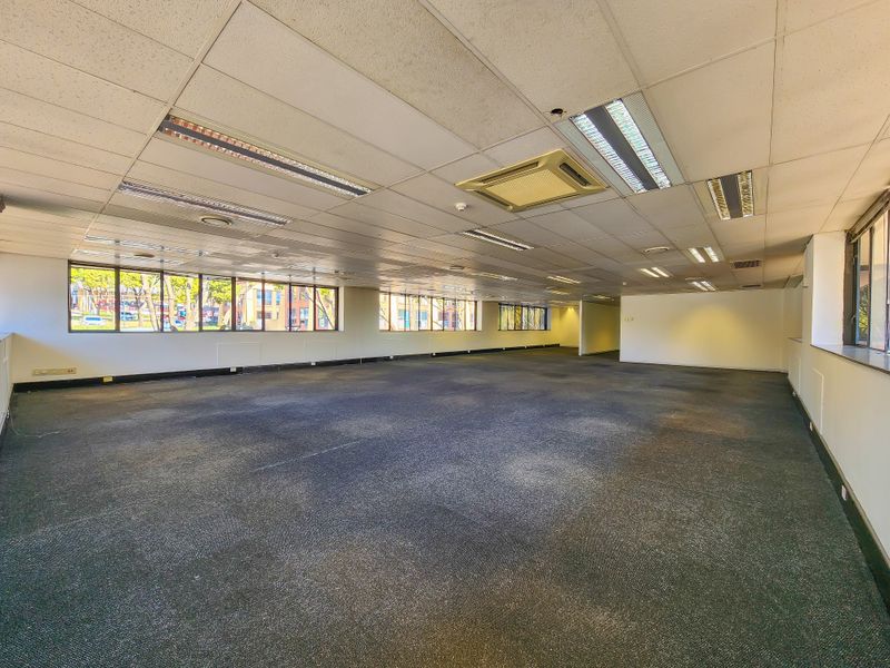 Spacious open-plan office area featuring suspended ceilings, recessed lighting, ducted air conditioning, and large windows providing ample natural light.