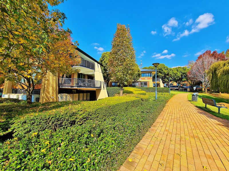 A well-maintained office complex exterior featuring paved walkways, manicured hedges, and multi-level balconies with brick architectural detailing.