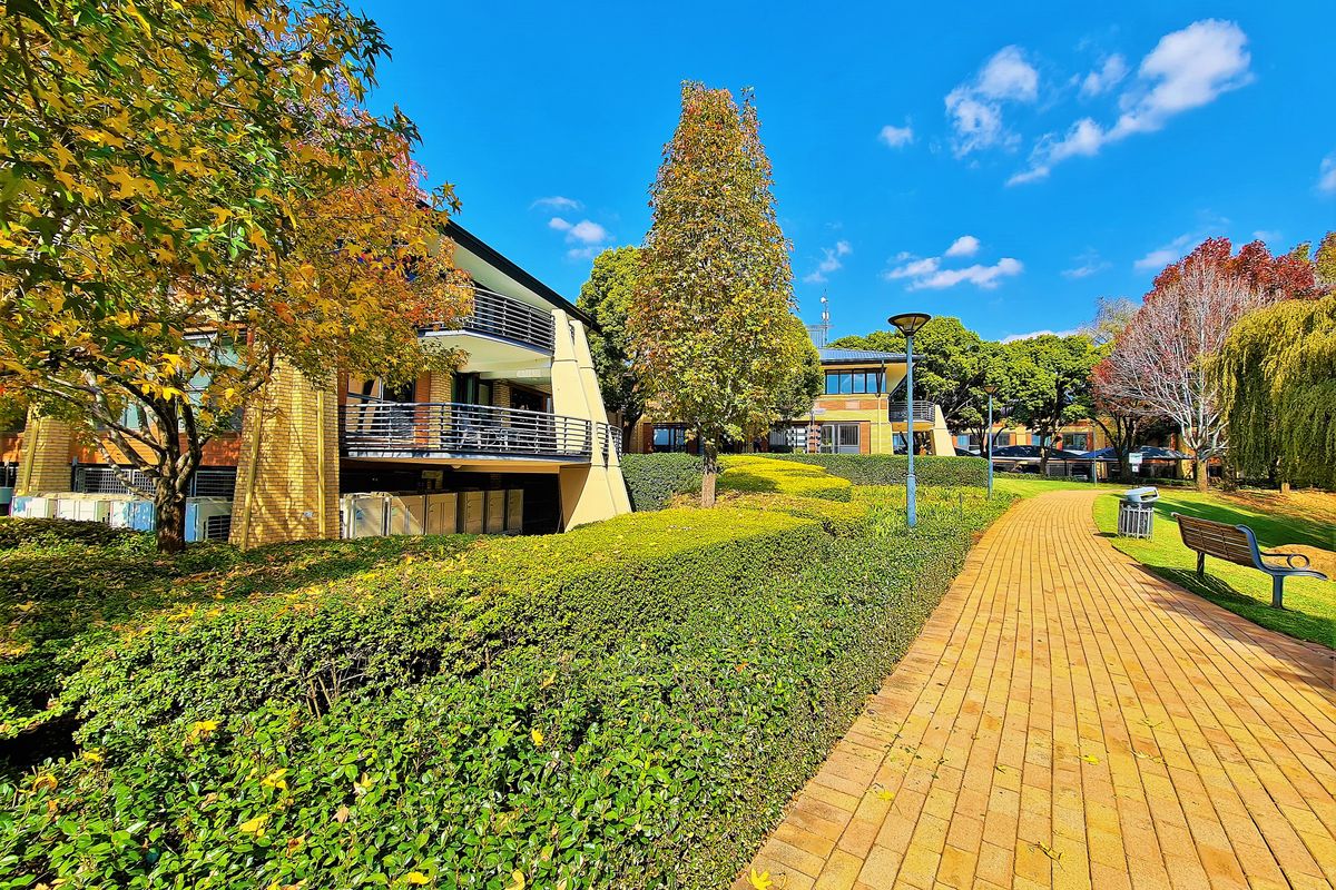A well-maintained office complex exterior featuring paved walkways, manicured hedges, and multi-level balconies with brick architectural detailing.