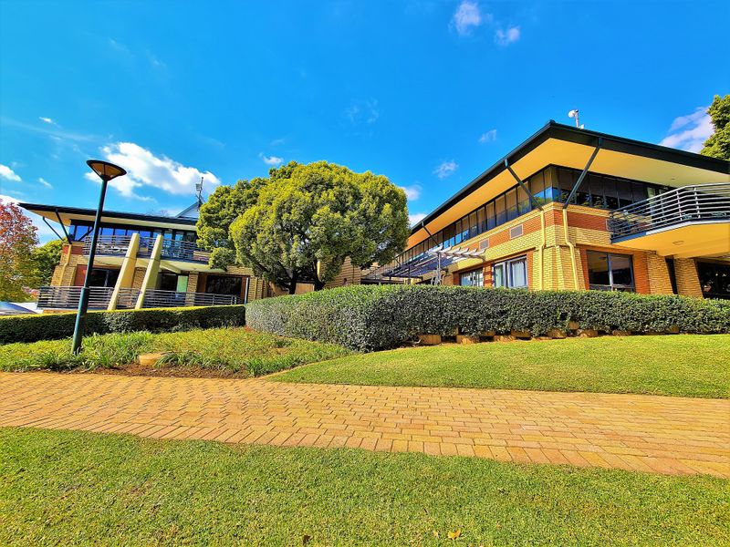 A well-maintained office building exterior featuring brick facade, multiple balconies with metal railings, and a landscaped garden with a paved walkway.