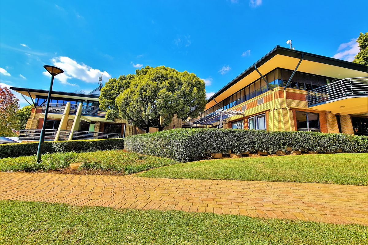 A well-maintained office building exterior featuring brick facade, multiple balconies with metal railings, and a landscaped garden with a paved walkway.