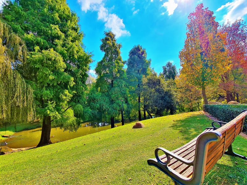 A well-maintained garden area featuring a lush green lawn, mature trees, and a scenic water feature, providing a tranquil outdoor environment.