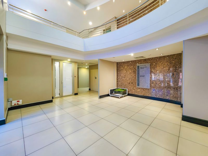 Spacious office building entrance lobby featuring tiled flooring, a mezzanine level with metal balustrades, and a prominent stone feature wall with directory signage.