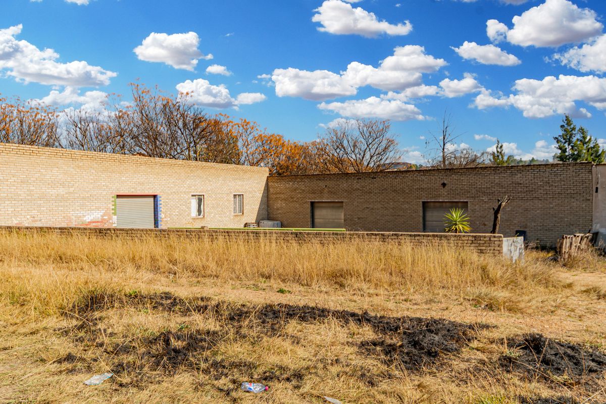 Rear view of a brick structure featuring multiple roller shutter doors and a surrounding boundary wall on a large plot.