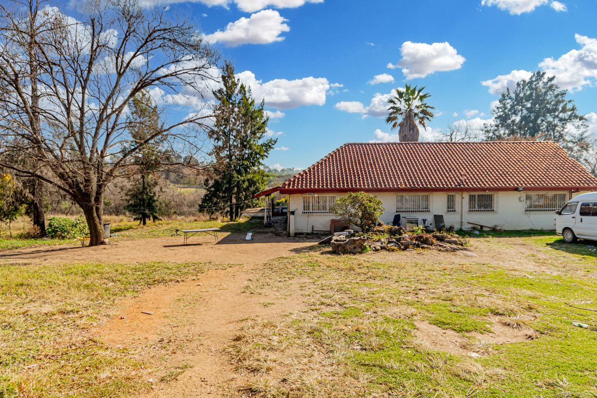 Rear view of a single-story small holding property featuring a terracotta tiled roof and security bars on windows, set on a large rural plot.