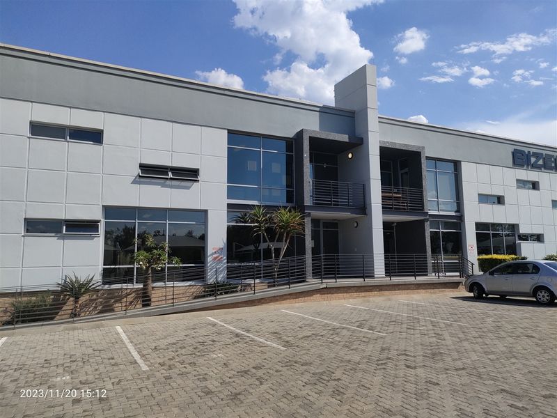 Modern industrial office building featuring a paved parking area, access ramp, large glass windows, and upper-level balconies with metal railings.