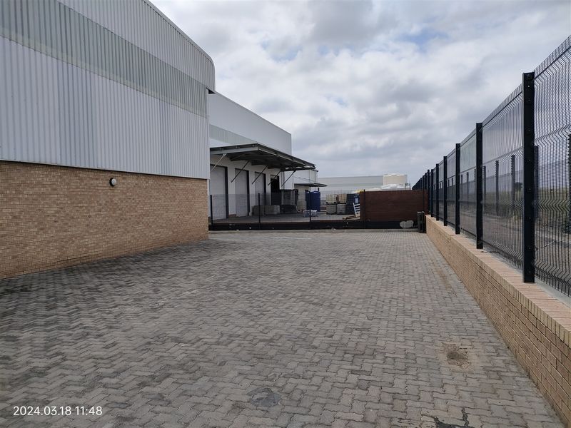 Rear industrial yard featuring paved driveway, secure perimeter fencing, brick boundary walls, and loading bay access with metal cladding.