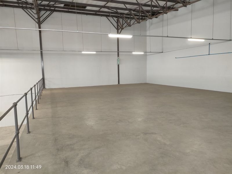 A spacious, open-plan industrial mezzanine area featuring concrete flooring, exposed steel roof trusses, and functional overhead strip lighting.