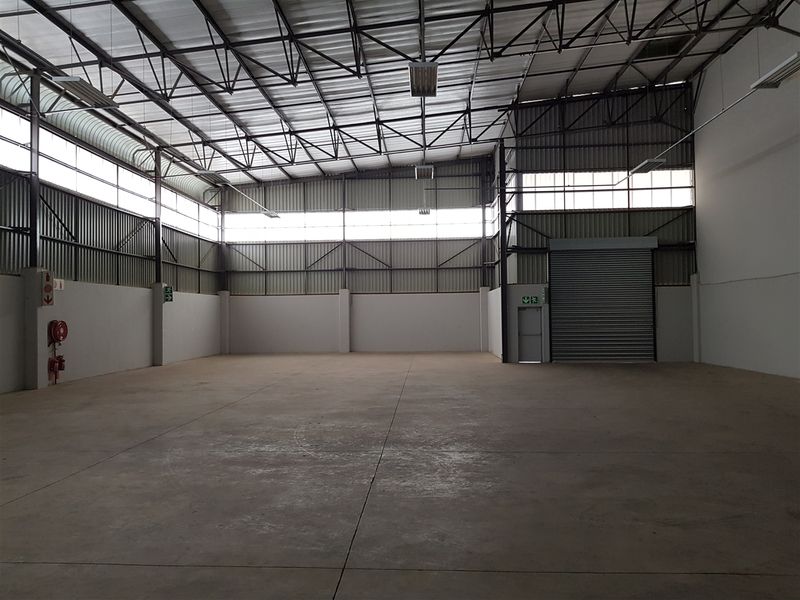 Spacious industrial warehouse unit featuring high ceilings with steel truss roofing, concrete flooring, and a large roller shutter door for easy access.