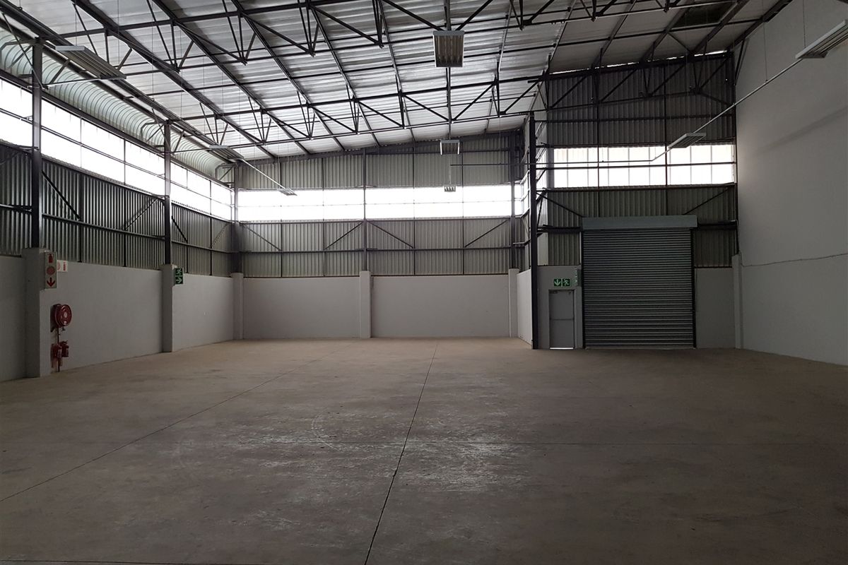 Spacious industrial warehouse unit featuring high ceilings with steel truss roofing, concrete flooring, and a large roller shutter door for easy access.