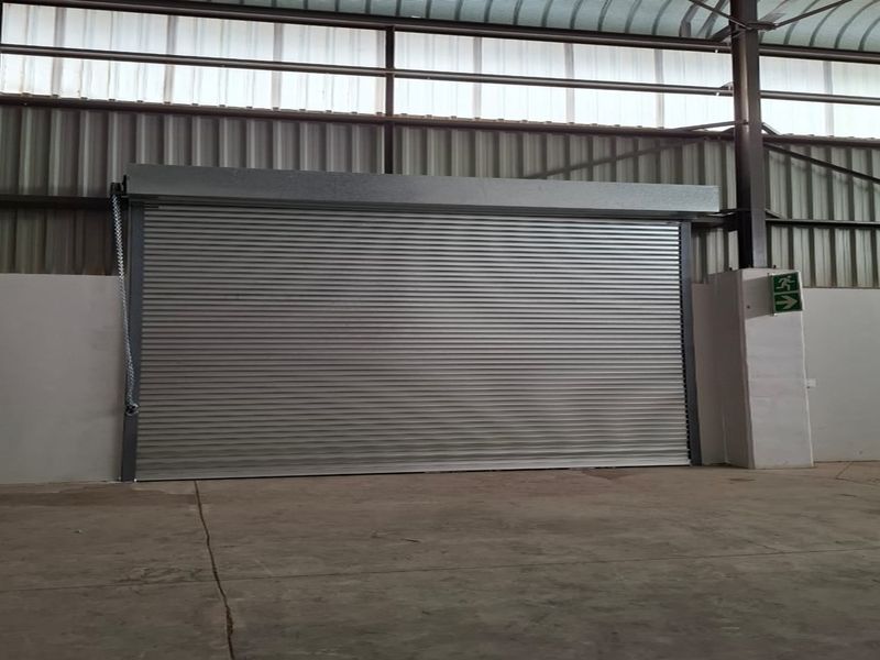 Industrial utility space featuring a large roller shutter door, concrete flooring, and exposed steel structural framing.