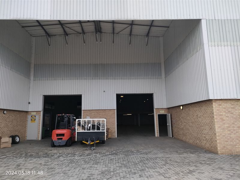 Industrial warehouse exterior featuring high-clearance roller shutter doors, face brick base, and corrugated metal cladding with a paved forecourt area.
