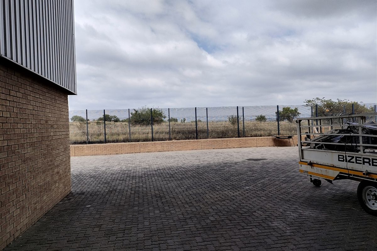 Rear exterior area of the industrial property featuring paved surfacing, brick retaining wall, and secure perimeter fencing.