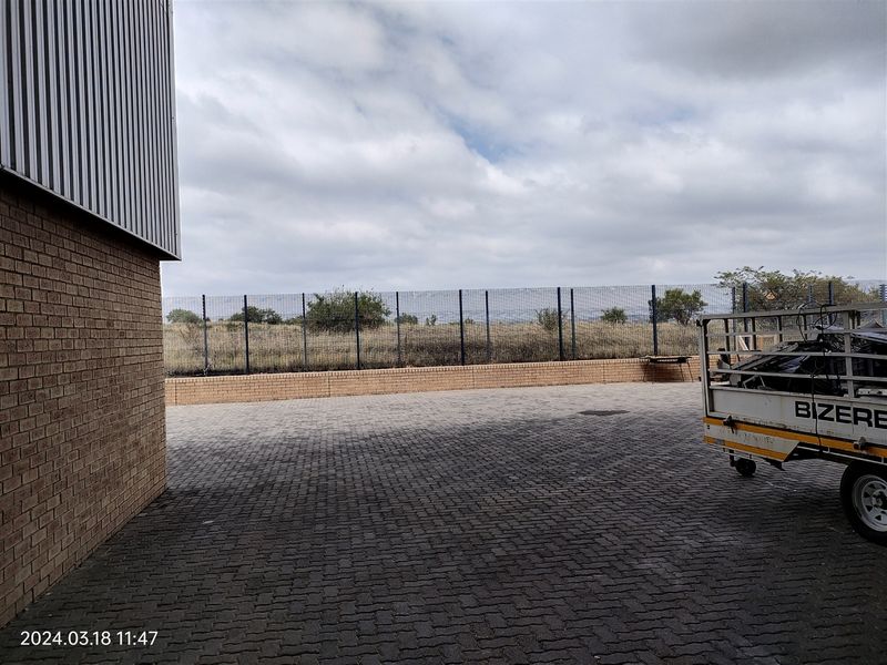 Rear exterior area of the industrial property featuring paved surfacing, brick retaining wall, and secure perimeter fencing.