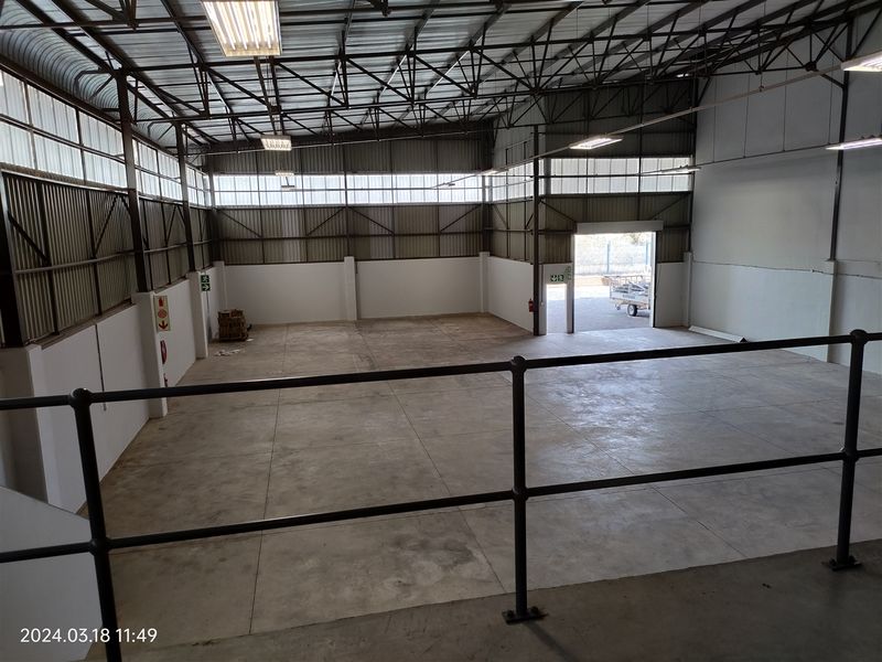 Spacious industrial warehouse unit featuring high ceilings with exposed steel trusses, concrete flooring, and large roller shutter access.