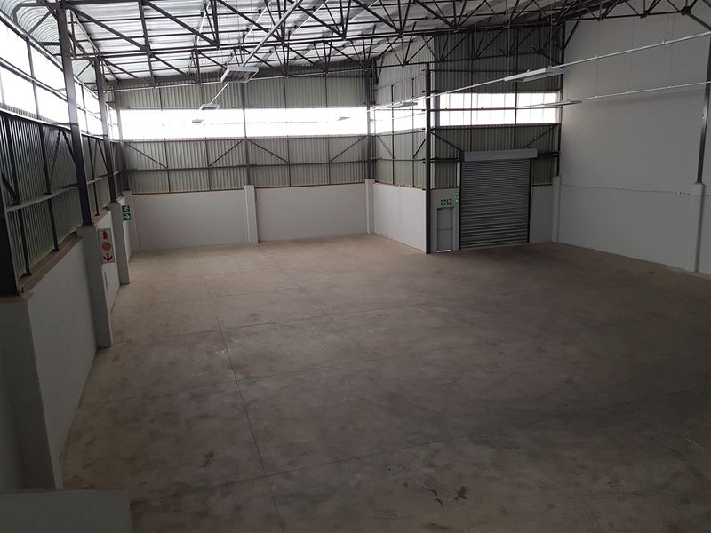 Spacious industrial warehouse unit featuring high ceilings with exposed steel trusses, concrete flooring, and a large roller shutter door for easy access.