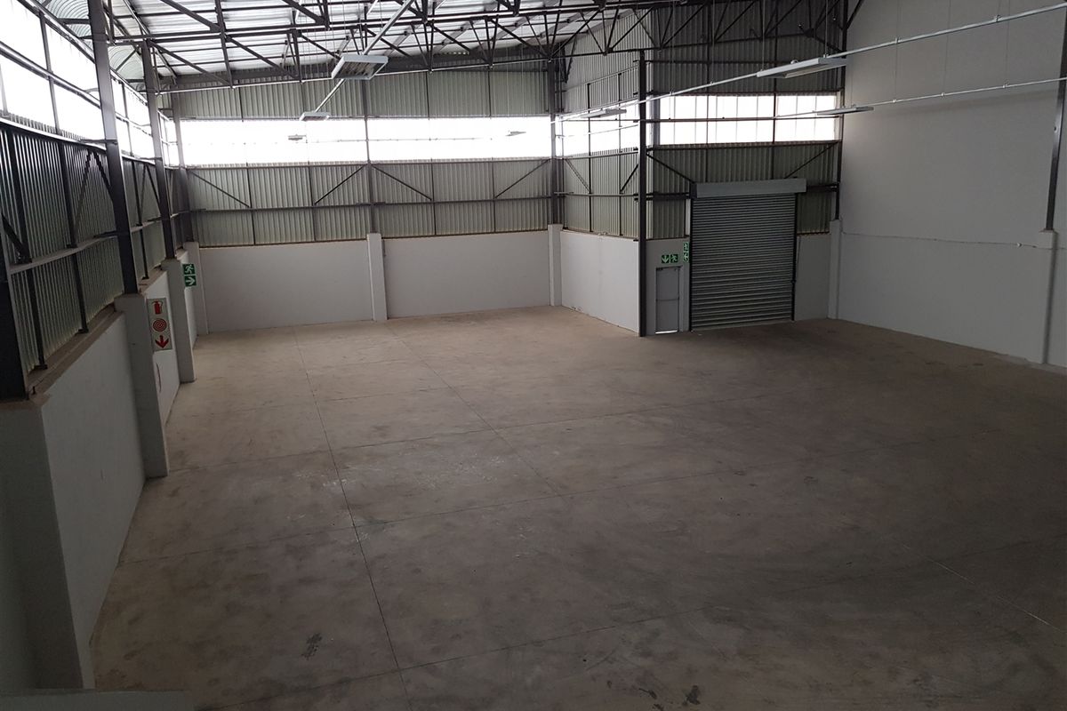 Spacious industrial warehouse unit featuring high ceilings with exposed steel trusses, concrete flooring, and a large roller shutter door for easy access.