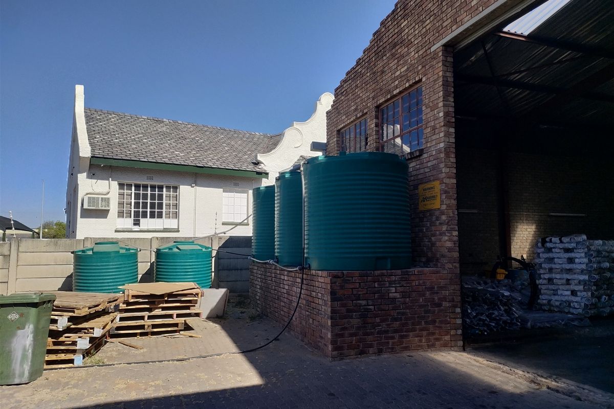 Exterior view of an industrial property featuring multiple large water storage tanks, brick facade, and an open-bay warehouse entrance.