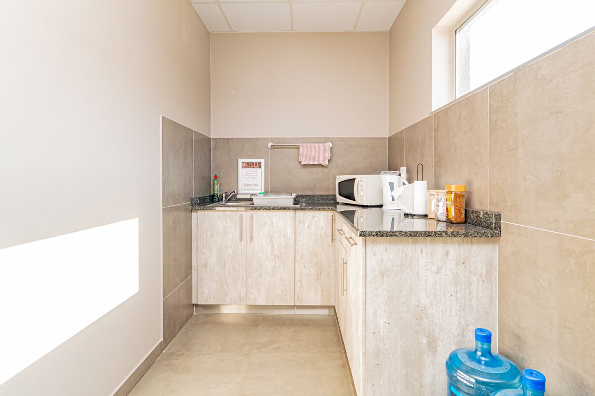 A functional kitchenette featuring granite countertops, laminate cabinetry, and tiled splashbacks, providing a clean and practical workspace for staff or office use.