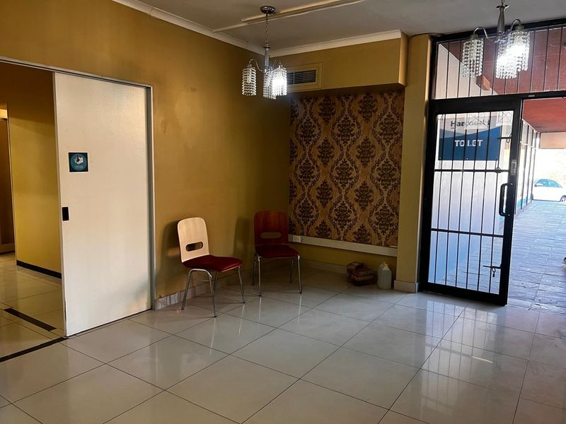 A functional retail entrance area featuring tiled flooring, a secure glass door, decorative wallpaper accents, and overhead lighting.