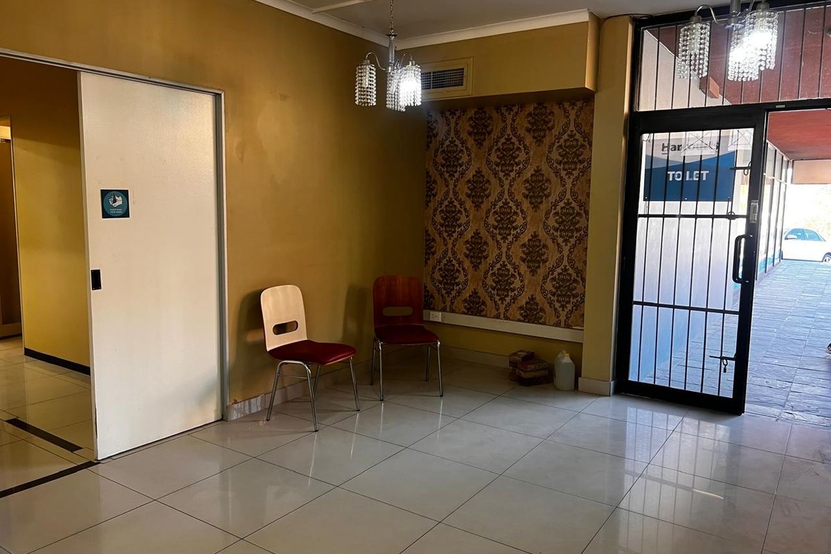 A functional retail entrance area featuring tiled flooring, a secure glass door, decorative wallpaper accents, and overhead lighting.