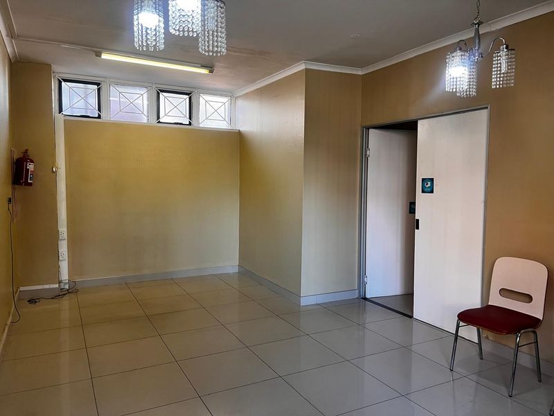 An empty, open-plan retail space featuring tiled flooring, crystal chandeliers, and high-level windows, suitable for a variety of commercial uses.