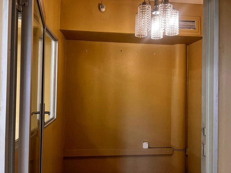 A small, empty interior space featuring mustard-colored walls, a crystal chandelier, and visible electrical conduit, suitable for various commercial uses.